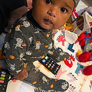 Jayden is registered to the contest to win money with this photo: baby, cap, child, closeup, colorful, curious, eyes, face, halloween, indoors, infant, patterned_clothing, person, play_mat, playroom, portrait, remote_control, sitting, skeleton_costume, toys