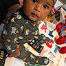 baby, cap, child, closeup, colorful, curious, eyes, face, halloween, indoors, infant, patterned_clothing, person, play_mat, playroom, portrait, remote_control, sitting, skeleton_costume, toys