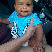 Jayden joined the competition — help win amazing prizes! baby, child, smiling, portrait, car, vehicle, indoors, sitting, blue_shirt, socks, adult_hand, family, infant, happy, face, dashboard, water_bottle, road_trip, daylight, candid