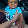 baby, child, smiling, portrait, car, vehicle, indoors, sitting, blue_shirt, socks, adult_hand, family, infant, happy, face, dashboard, water_bottle, road_trip, daylight, candid
