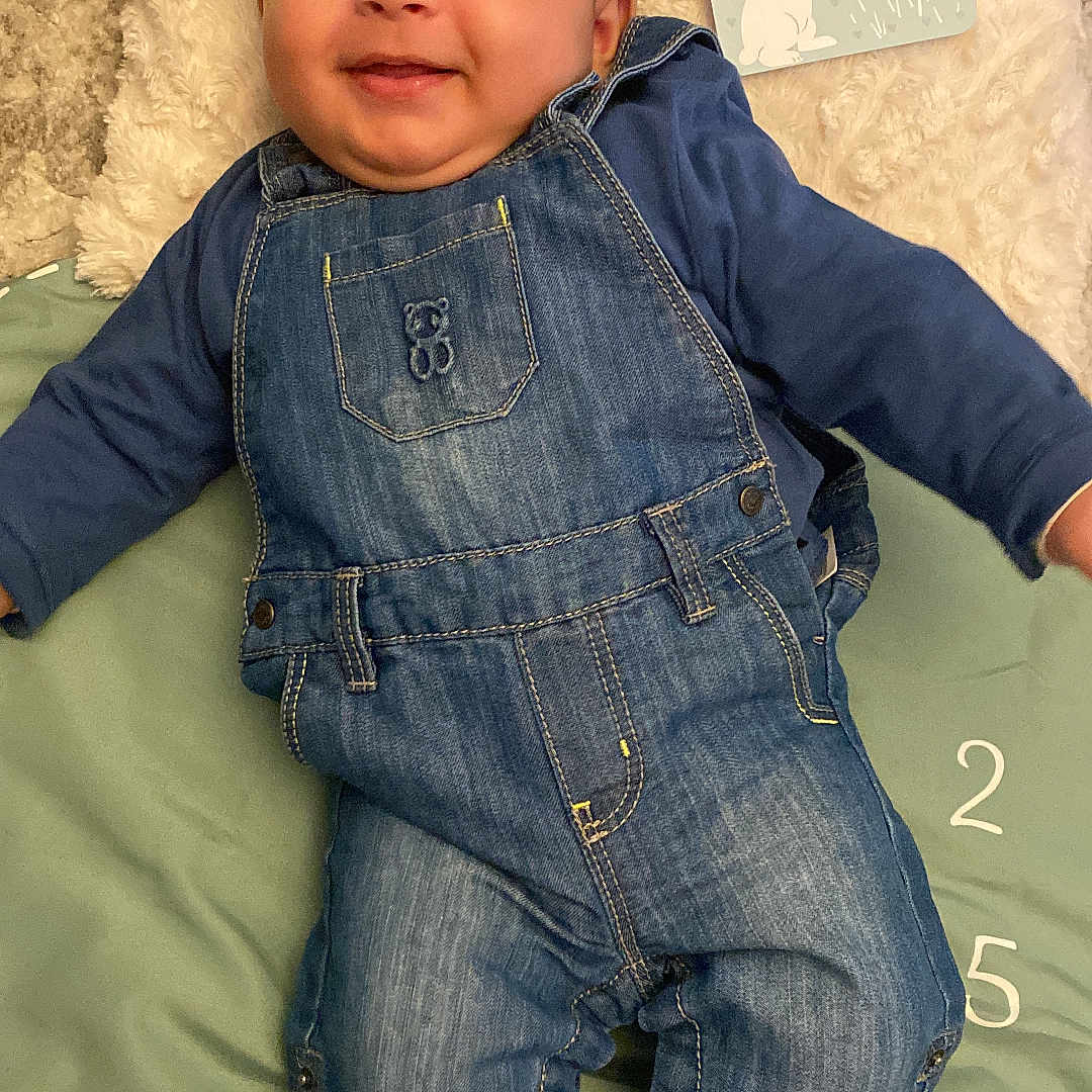 Ismaïl participe au concours pour gagner de l'argent avec cette photo : baby, bodypart, clothing, coat, couch, face, finger, furniture, happy, head, hosiery, jacket, jeans, pants, person, photography, portrait, smile, sock, vest