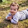 baby, child, smiling, grass, outdoor, sunlight, happy, young, nature, flower, casual_clothing, face, person, portrait, greenery, daylight, cute, lying_down, toddler, playful
