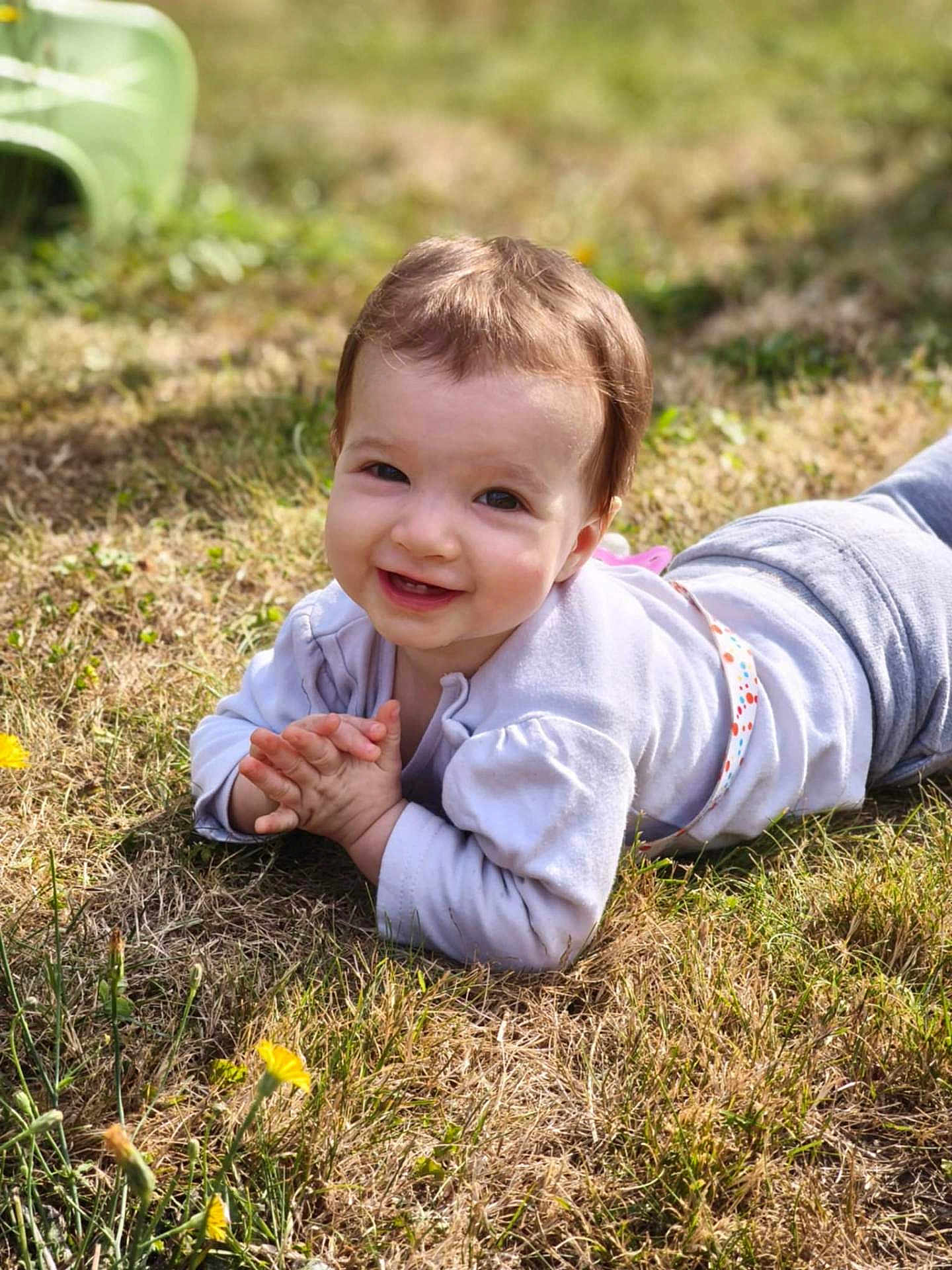 Clémence a rejoint le concours — aidez-le/la à gagner de superbes lots ! baby, child, smiling, grass, outdoor, sunlight, happy, young, nature, flower, casual_clothing, face, person, portrait, greenery, daylight, cute, lying_down, toddler, playful