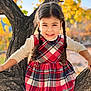 child, girl, braids, plaid_dress, long_sleeve_shirt, tree, tree_branch, autumn, fall_foliage, smiling, outdoor, nature, portrait, happy, young_child, daylight, casual_clothing, cute, seasonal, park