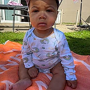 Soren participe au concours pour gagner de l'argent avec cette photo : baby, child, outdoor, grass, blanket, cap, onesie, sunlight, basketball_hoop, garden, fence, patio, table, chair, person, foot, hand, face, expression, summer