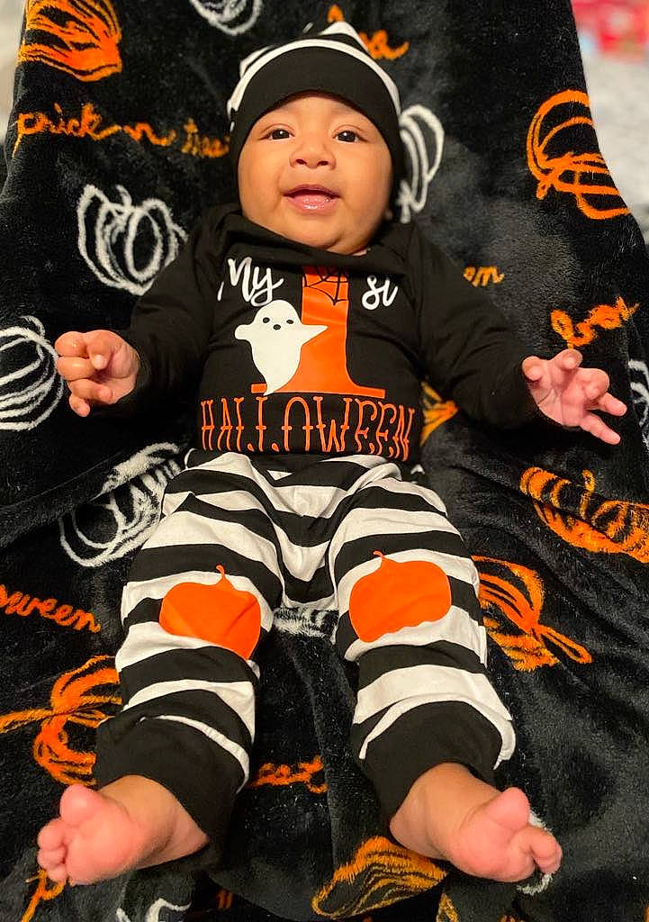 Oliver is registered to the contest to win money with this photo: baby, baby_toddler_clothing, black, cap, child, font, glove, hat, headgear, headwear, jersey, orange, outerwear, pattern, person, sitting, sleeve, sock, sportswear, t_shirt