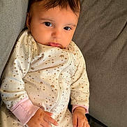Rose joined the competition — help win amazing prizes! baby, child, infant, portrait, sitting, couch, gray_couch, onesie, pajamas, patterned_clothing, long_sleeves, pink_cuffs, dark_hair, brown_eyes, wide_eyed, looking_at_camera, indoors, soft_lighting, close_up, adorable