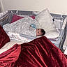 Rose is registered to the contest to win money with this photo: baby, infant, child, crib, bedding, blanket, pillow, sleeping, lying_down, indoor, nursery, home, portrait, face, eyes, hair, cozy, red_blanket, furniture, photography