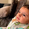 baby, infant, child, portrait, face, eyes, smiling, indoor, couch, cushions, blanket, clothing, onesie, patterned_clothing, cartoons, colorful, sitting, close_up, home, relaxed