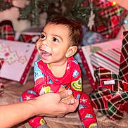 Kyson joined the competition — help win amazing prizes! baby, child, smiling, pajamas, holiday, christmas_tree, presents, gift_wrap, indoor, floor, hand_holding, happy, festive, celebration, person, cute, face, sitting, toy, home