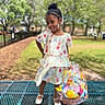 child, girl, smiling, floral_dress, easter_basket, outdoor, park, bench, spring, happy, holding, fashion, footwear, hair_bun, accessory, nature, greenery, sunlight, playful, cute