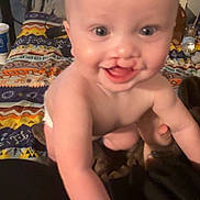 Horace is registered to the contest to win money with this photo: baby, blanket, child, cute, diaper, expression, eyes, face, floor, hand, happy, indoor, infant, mouth, patterned_blanket, person, reaching, skin, smiling, young_child