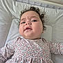 baby, child, curly_hair, floral_dress, cushion, white_background, face, skin, expression, lying_down, infant, portrait, indoors, cute, person, head, clothing, young_child, health, closeup