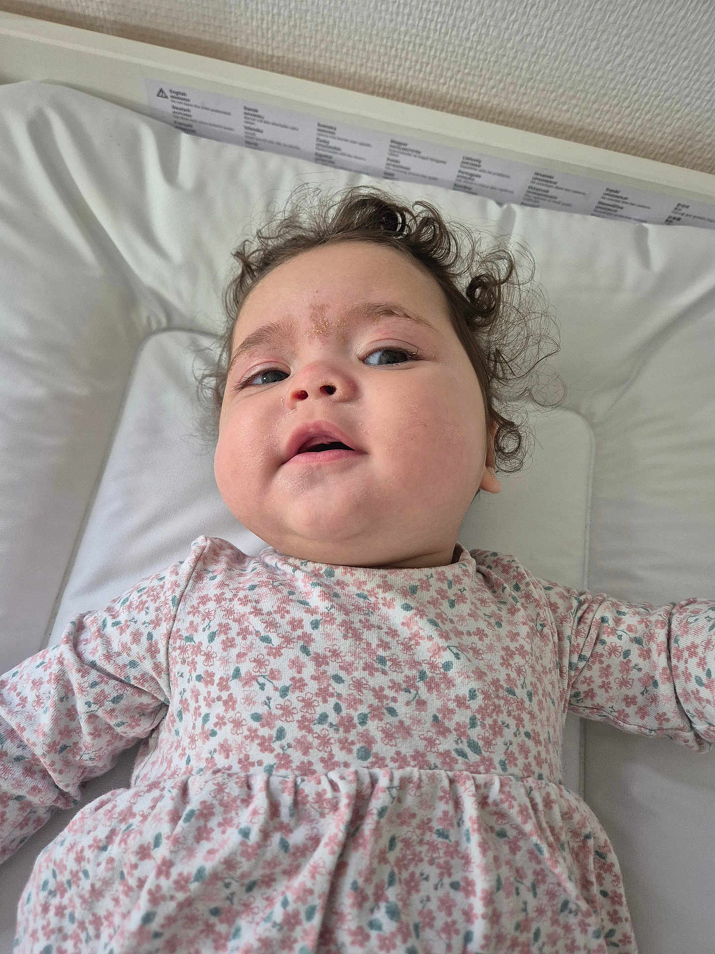 Mia participe au concours pour gagner de l'argent avec cette photo : baby, child, curly_hair, floral_dress, cushion, white_background, face, skin, expression, lying_down, infant, portrait, indoors, cute, person, head, clothing, young_child, health, closeup