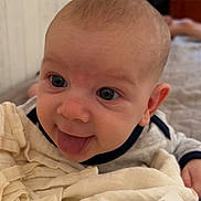 Arthur a rejoint le concours — aidez-le/la à gagner de superbes lots ! baby, child, tongue, blanket, bed, indoors, soft_fabric, person, infant, playful, cute, face, light, blurred_background, clothing, room, head, skin, expression, smile