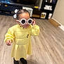 toddler, child, indoor, floor, yellow_dress, sunglasses, hair_bow, boots, person, smiling, cute, fashion, standing, wood_floor, furniture, shelf, home, playful, portrait, accessory