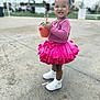 toddler, child, pink_tutu, white_sneakers, strawberry_cup, outdoor, concrete, smiling, standing, person, cute, fashion, happy, playful, daylight, grass_background, short_hair, casual, young_child, portrait