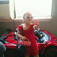 Ashley joined the competition — help win amazing prizes! accessories, bright_light, casual, child, colorful, cute, fashion, fun, handbags, heart_shaped_sunglasses, indoor, playful, portrait, posing, red_dress, room, smile, toy_car, window, young_girl