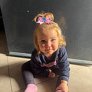 Maëna participe au concours pour gagner de l'argent avec cette photo : child, toddler, girl, pink_bow, sweatshirt, socks, floor, tile, indoor, smile, face, hair, blonde, light, shadow, sitting, casual_clothing, person, cute, young