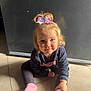 child, toddler, girl, pink_bow, sweatshirt, socks, floor, tile, indoor, smile, face, hair, blonde, light, shadow, sitting, casual_clothing, person, cute, young