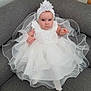 Maëna participe au concours pour gagner de l'argent avec cette photo : baby, child, white_dress, headband, couch, gray_couch, frilly_dress, infant, portrait, sitting, cute, serious_expression, indoors, fabric, clothing, person, young_child, fashion, elegant, adorable