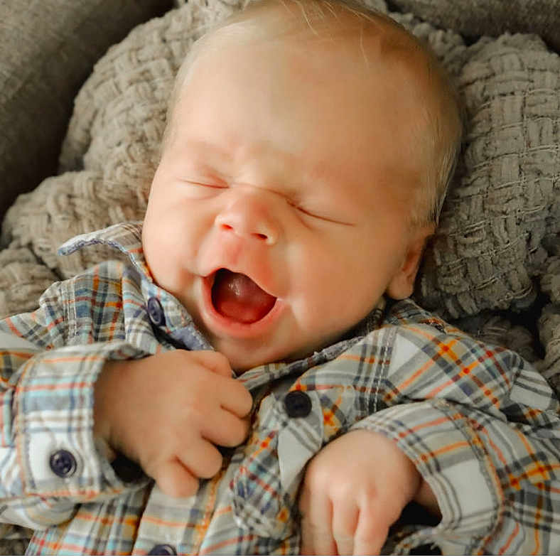 Doyle is registered to the contest to win money with this photo: baby, blanket, child, cozy, cute, expression, face, hands, happy, indoor, infant, knit, mouth_open, newborn, plaid_shirt, portrait, skin, sleepy, smiling, soft_light