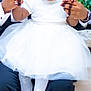 child, man, tuxedo, white_dress, holding_hands, smile, sitting, formal, portrait, indoor, curly_hair, flower_decor, white_shoes, stockings, black_jacket, happy, family, celebration, people, cute
