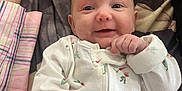 Leila is registered to the contest to win money with this photo: baby, infant, smile, onesie, hand, blanket, pattern, person, cute, lying_down, clothing, newborn, face, skin, child, happy, indoors, soft, comfort, support