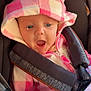 Leila is registered to the contest to win money with this photo: baby, child, infant, car_seat, hoodie, pink, white, checkered_pattern, ears, blanket, face, open_mouth, clothing, seatbelt, cute, young, expression, portrait, warm, indoor