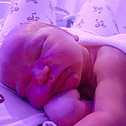 Eli is registered to the contest to win money with this photo: newborn, baby, sleeping, blanket, purple_light, peaceful, face, hand, infant, soft_light, bed, patterned_fabric, skin, resting, closeup, cozy, indoors, quiet, calm, portrait