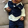 baby, child, smiling, face, vest, bow_tie, pants, shirt, couch, indoor, person, happy, clothing, footwear, sitting, portrait, cute, infant, black_hair, hands