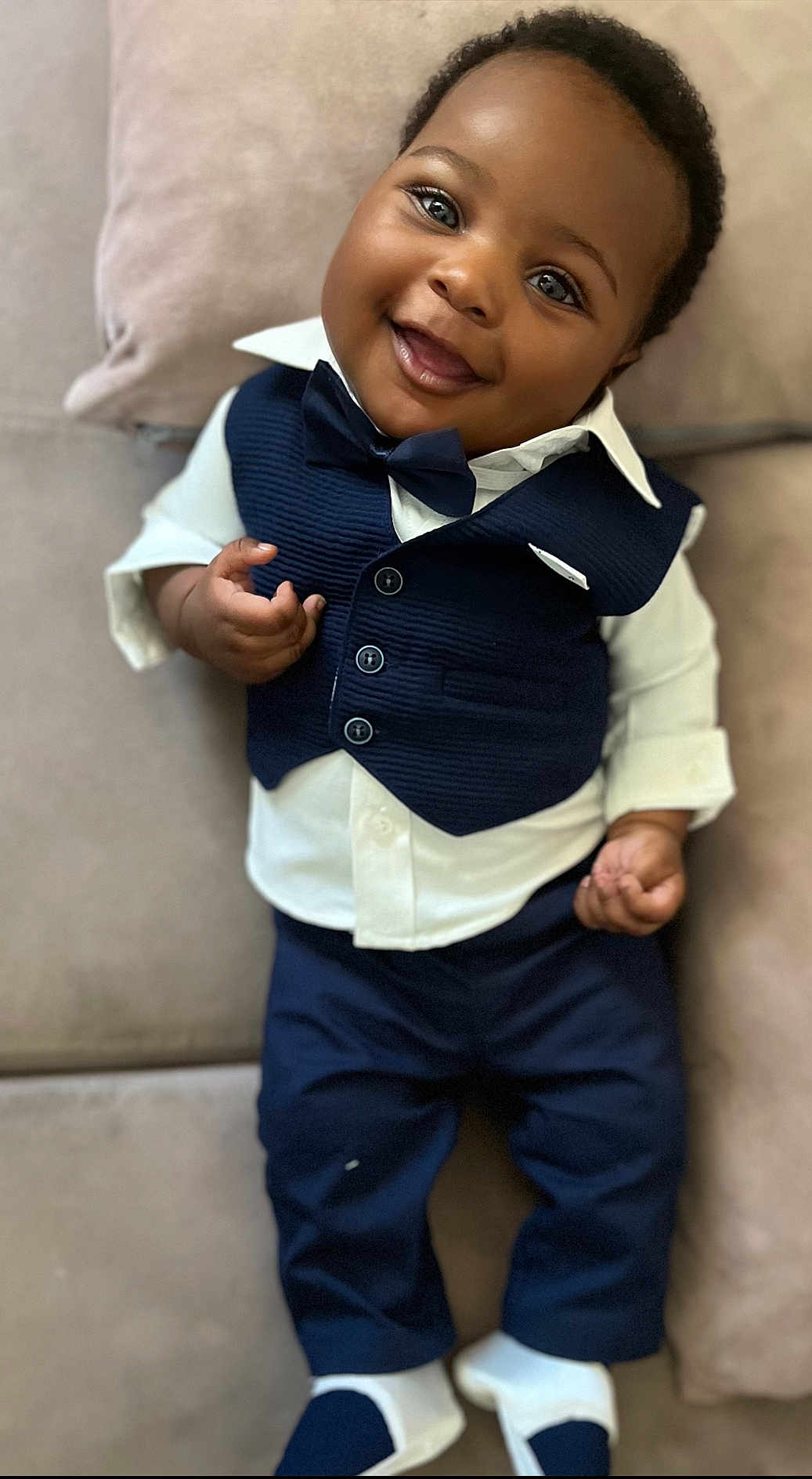 Jelany a rejoint le concours — aidez-le/la à gagner de superbes lots ! baby, child, smiling, face, vest, bow_tie, pants, shirt, couch, indoor, person, happy, clothing, footwear, sitting, portrait, cute, infant, black_hair, hands