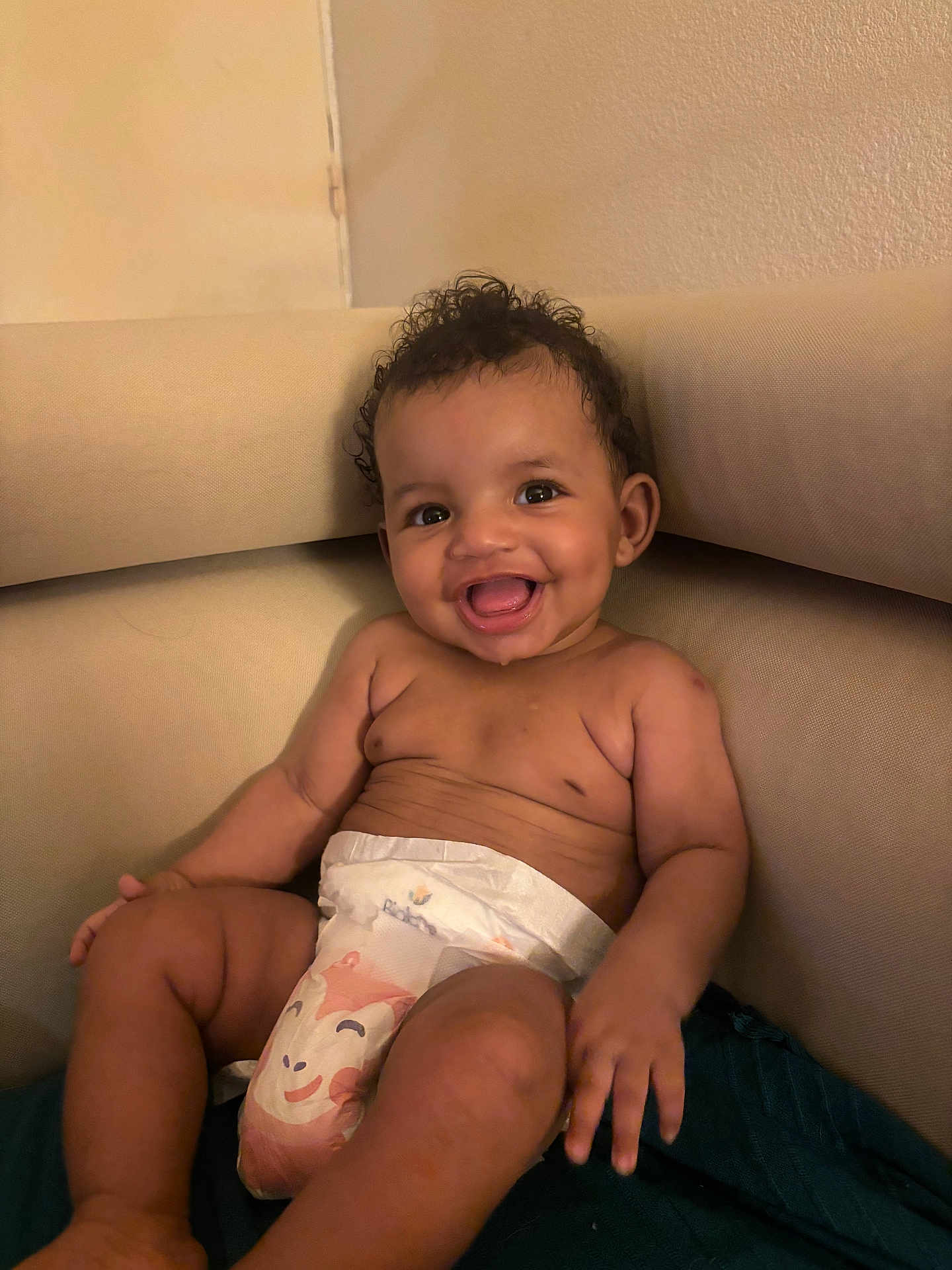 Vanessa participe au concours pour gagner de l'argent avec cette photo : baby, smiling, diaper, curly_hair, dimples, couch, indoor, happy, child, person, skin, young, seated, infant, cute, portrait, furniture, relaxing, comfort, toddler