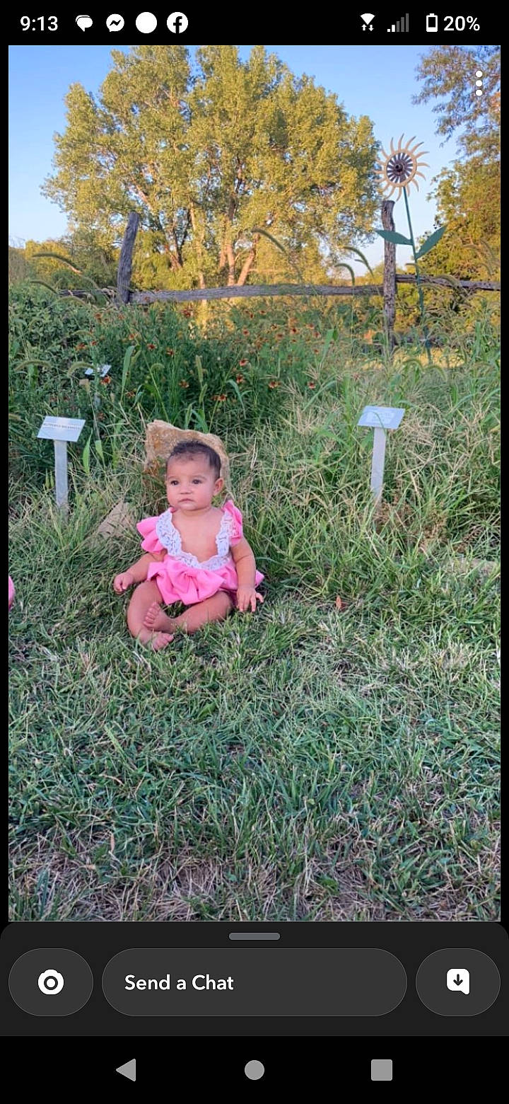 Elda is registered to the contest to win money with this photo: baby_toddler_clothing, grass, grass_family, grassland, happy, landscape, leaf, magenta, meadow, natural_environment, natural_landscape, people_in_nature, person, plant, prairie, sitting, sky, soil, terrestrial_plant, toddler