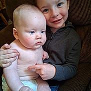 Randy joined the competition — help win amazing prizes! baby, child, sibling, couch, diaper, smile, blue_eyes, casual_clothing, indoor, family, holding, cute, skin, expression, seated, person, young_child, toddler, affection, cozy