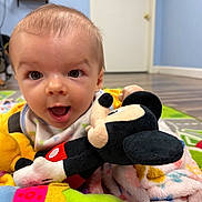 Tristan joined the competition — help win amazing prizes! baby, child, plush_toy, mickey_mouse, blanket, play_mat, indoor, floor, happy, cute, person, toy, colorful, smiling, infant, head, face, clothing, room, wooden_floor