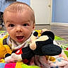 baby, child, plush_toy, mickey_mouse, blanket, play_mat, indoor, floor, happy, cute, person, toy, colorful, smiling, infant, head, face, clothing, room, wooden_floor