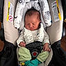 newborn, baby, sleeping, infant, car_seat, harness, buckled, portrait, face, closed_eyes, indoors, cushion, padding, clothing, green_pants, socks, colorful, safe, seated, photography