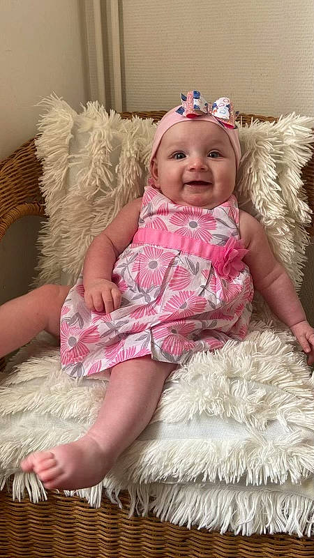 Calista a rejoint le concours — aidez-le/la à gagner de superbes lots ! baby, baby_toddler_clothing, blond, child, couch, dress, embellishment, face, facial_expression, happy, headgear, headwear, joy, magenta, pattern, person, pink, sitting, skin, sleeve