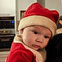 baby, child, santa_hat, red_clothing, holiday, christmas, indoors, kitchen, face, portrait, cute, expression, soft_lighting, close_up, person, festive, winter_clothing, young_child, holding, warm