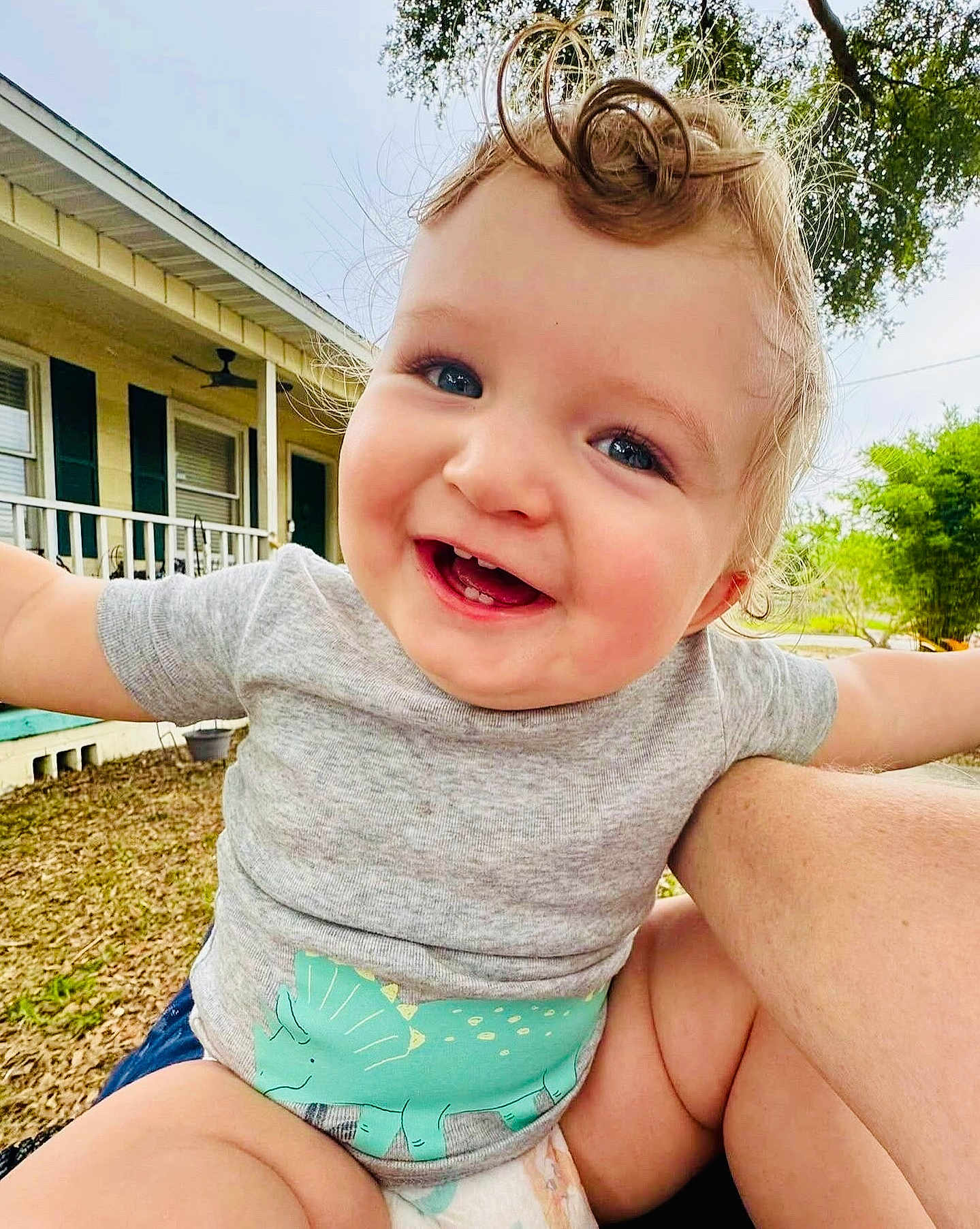 Eros joined the competition — help win amazing prizes! baby, child, smiling, curly_hair, dinosaur_print, grey_shirt, outdoor, yard, house, grass, tree, happy, arms_outstretched, diaper, person, cute, portrait, daylight, closeup, face