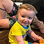 Eros joined the competition — help win amazing prizes! baby, child, yellow_clothing, plush_toy, giraffe_toy, indoor, blanket, tattoo, adult, person, smiling, happy, sitting, floor, shorts, patterned_clothing, face, head, arm, playful