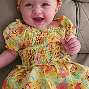 Charlotte joined the competition — help win amazing prizes! baby, child, smiling, dress, headband, yellow, cartoon_print, sitting, couch, leather, happy, portrait, indoor, cute, infant, person, clothing, colorful, face, young