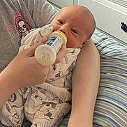 Weston joined the competition — help win amazing prizes! baby, bottle, feeding, infant, onesie, animal_print, person, hand, arm, bed, pillow, striped, indoor, closeup, newborn, comfort, caring, feeding_time, sleepwear, nursery