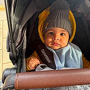 Isaiah is registered to the contest to win money with this photo: baby, stroller, hat, pom_pom, blanket, yellow_jacket, child, face, hand, outdoor, clothing, cute, infant, portrait, seat_belt, warm_clothing, baby_carrier, expression, person, closeup