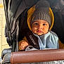 baby, stroller, hat, pom_pom, blanket, yellow_jacket, child, face, hand, outdoor, clothing, cute, infant, portrait, seat_belt, warm_clothing, baby_carrier, expression, person, closeup