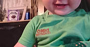 Oaklee is registered to the contest to win money with this photo: adult_arm, baby, casual, child, cute, family, frame, furniture, green_shirt, happy, holding, home, indoor, person, plant, portrait, shelf, smiling, toddler, wood