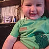 toddler, child, smiling, green_shirt, person, indoor, adult_arm, home, shelf, frame, plant, wood, furniture, portrait, happy, cute, casual, baby, holding, family