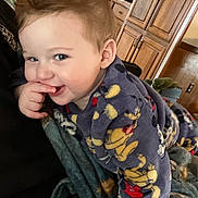 Oaklee is registered to the contest to win money with this photo: toddler, child, pajamas, mickey_mouse, smile, finger_in_mouth, blanket, indoor, wooden_cabinets, cozy, playful, cute, face, blue_eyes, hair, furniture, home, person, portrait, young_child