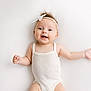 Ava participe au concours pour gagner de l'argent avec cette photo : arms_outstretched, baby, baby_girl, child, cute, expression, face, happy, headband, human, infant, lying_down, onesie, portrait, skin, smiling, soft_lighting, studio_photo, white_background, white_clothing
